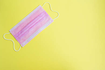 One surgical medical mask on a yellow background.