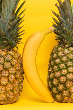 Pineapples with a banana on a yellow background.の写真素材
