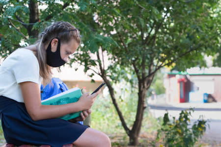Schoolgirl girl on the street with a textbook and in a protective mask