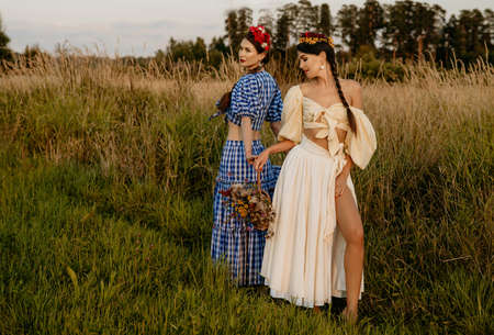 Young girls dressed in white and blue dress pose against the background of nature, and hold a basket of flowers in their hands.の写真素材