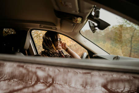 A young beautiful girl in a headscarf is sitting in an expensive brown car.の写真素材