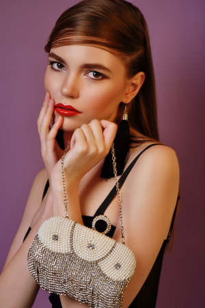 A young beautiful girl posing in a black leather jacket and gold jewelry on a background in a photo...