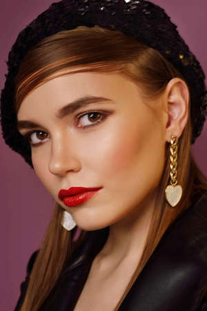 A young beautiful girl posing in a black leather jacket and gold jewelry on a background in a photo...