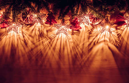 Christmas hygge background, upper border with spruce tree branches star shape party lights...