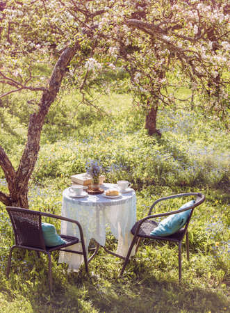 Springtime in garden. Table set with tea cups, boho reuse jar vase with forget me not flowers(...