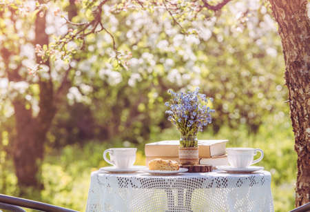 Springtime in garden. Table set with tea cups, boho reuse jar vase with forget me not flowers(...
