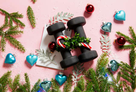 Flat lay view of black dumbbells with white spiral notebook with Christmas ornaments on pink background. Healthy lifestyle during Christmas feasting period concept.の写真素材