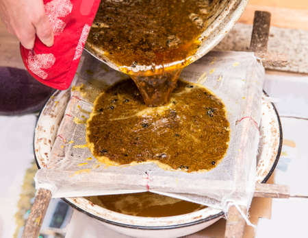 Close up view of beekeeper pouring melted beeswax (cera alba) through gauze filter to clean old used...