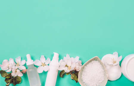 Top view of generic clean pure spring beauty products background with copy space, room for text in the middle. White containers, mint green background, white tender apple tree blossoms for decoration.の写真素材