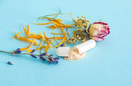 Side view of single white color gel capsule opened, yellow powder spilled out, on light blue...