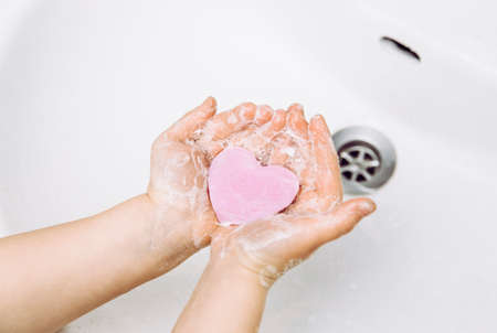 Importance of personal hygiene care. Flat lay view of child washing dirty hands with pink heart shape soap bar, lot of foam. Copy space.の写真素材