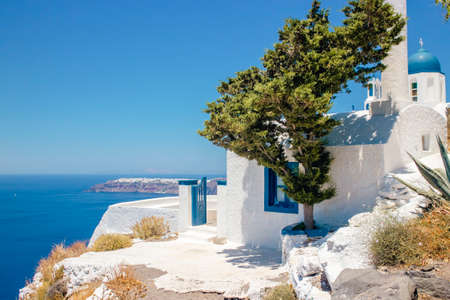 Selective focus on blue dome church (Theoskepasti) on the side of the Skaros Rock on volcanic island of Santorini in Greece, Europe. City of Oia on caldera cliff on the background.のeditorial素材