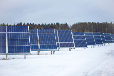 Industrial solar power farm station on field in rural area in winter, snow on ground, cloudy...