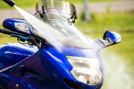 Close up view of using pressure washer to clean motorbike in home garden, green grass on background, summer day.の写真素材