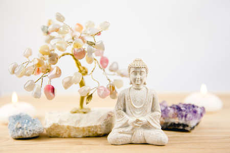 Calming meditation background with sitting meditating Buddha, crystal clusters( purple amethyst and blue celestite, celestine) and gemstone wire tree white minimalist background with copy space.の写真素材