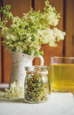 Fresh Meadowsweet, Filipendula ulmaria in jug shape vase and it`s herbal tea in glass, tea powder in...