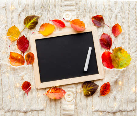 Flat lay view of empty black chalkboard on white knitted background for making autumn list, card or...