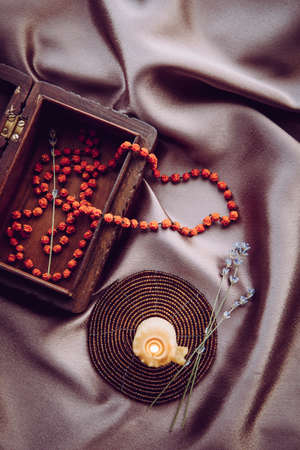 Necklace made of dried rowan berries, folklore protection spell charm concept. Beeswax candle burning and chain hanging out of brown wood decorative box.の写真素材