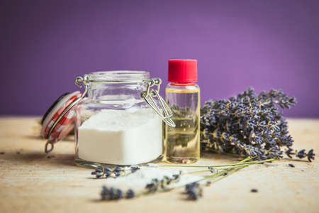 Olive oil and baking soda exfoliating scrub concept. Homemade natural beauty cosmetics. Jar with baking soda powder and bottle with olive oil, lavender bouquet on purple background.の写真素材