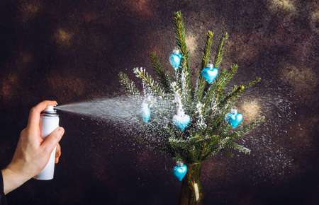 Close up view of person hand using canned spray snow to spray decorate Christmas tree branches in...