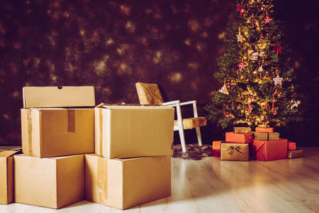 Moving in to new home for Christmas concept. Focus on cardboard relocation boxes and decorated Christmas tree with presents under it on the background. Copy space on black background.の写真素材