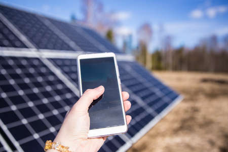 Person looking smartphone screen outdoors on field with solar panels station farm on background. Checking app.の写真素材