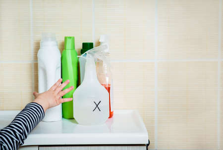 Child`s hand reaches out to household chemicals. Keep away from children. Safety Hazard for kids at home.の写真素材