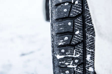 Closeup view of car tire with metal studs pikes outdoors on snowy icy road outdoors in winter. Helps stop and control car better on icy roads concept.の写真素材