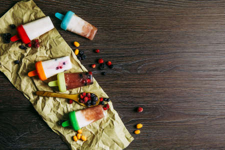 Flat lay view of lot of home made fridge frozen smoothie yogurt juice ice creams with wild berries on dark dramatic wooden background. Healthy snack concept, great for children.の写真素材