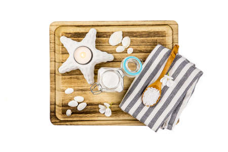 Flat lay view of ocean theme set of sea salt in glass jar and on wooden spoon on wooden tray, candle burning, seashells for decoration, isolated on white. Beauty and food concept.の写真素材