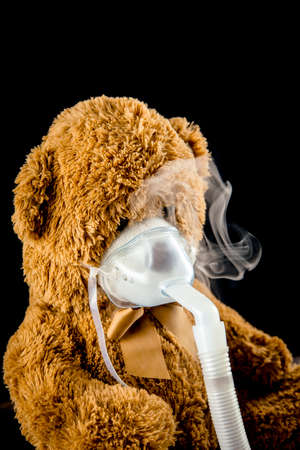 Steam mist from Nebulizer or nebuliser electrical machine drug delivery device used to administer medication in the form of a mist inhaled into the lungs concept. Toy teddy bear with face mask.の写真素材