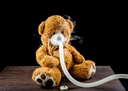 Steam mist from Nebulizer or nebuliser electrical machine drug delivery device used to administer medication in the form of a mist inhaled into the lungs concept. Toy teddy bear with face mask.の写真素材