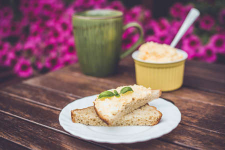 Yellow delicious egg and mayonnaise paste on whole wheat bread, breakfast snack recipe, pink flowers on the background, wooden base.の写真素材