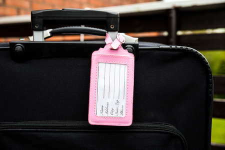 Pink feminine empty luggage tag attached to black baggage suitcase, fill in the tag, name, address, phone text. Lost, found design element concept.の写真素材