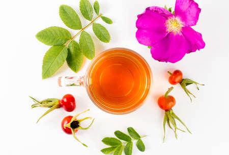 Flat lay view of the rose hip or rosehip, also called rose haw and rose hep tea in clear glass cup, raw berries, blossom and leaves for decoration on white background. Minimal composition.の写真素材