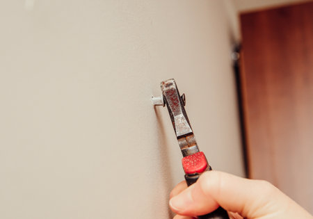 Close up view of person hand removing old plastic dowel, nylon wall plug from drywall with pliers at...