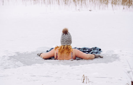 Woman wearing wool hat, mittens gloves and swimsuit, swimming dipping inside homemade ice hole in lake. Healthy winter ice bath concept.の写真素材