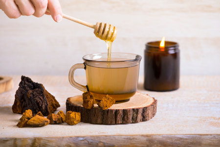 Dripping honey inside tea made with Chaga mushroom powder (Inonotus obliquus). Minimal wood background, studio shot.の写真素材