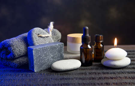 Group of different spa essentials, beard oil, gray soap, natural loofah sponge, candle, aroma oil on wooden and black background. Father, brother or husband gift idea concept. Blue color back light.の写真素材