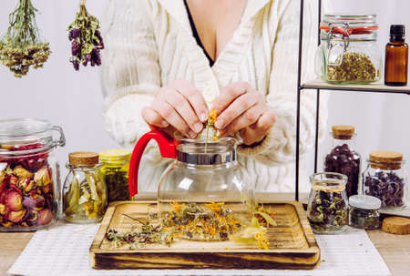 Close up view of woman herbalist mixing various dried herbs for traditional medicinal tea. Dried herbs in glass jars on background.の写真素材