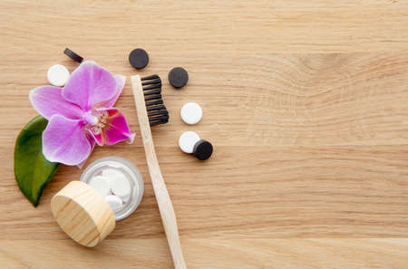 Top view of black activated charcoal and white fluoride toothpaste tablets. Dental care concept. Minimalist wood background with pink orchid flower, green leaf and glass jar for decoration.の写真素材