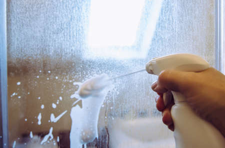 Person hand using limescale remover chemical foam. Descaling shower case glass door. Work in progress.