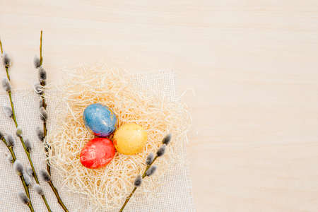 Three Easter eggs in nest with Pussy willow branches for decoration, lot of copy space on beige wood background.の写真素材