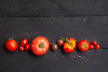Different shape, size and color fresh shiny tomatoes in a row, with lot of copy space on black color background. Room for text.の写真素材