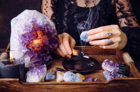 Glamorous woman in black dress cleansing crystals gemstones by smudging Palo Santo wood stick. Remove negative energy.の写真素材