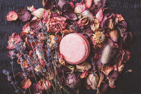 Pink color solid shampoo, conditioner bar on various dried multi color flower petals, rose, lavender. Romantic vintage matte style beauty set indoors.の写真素材