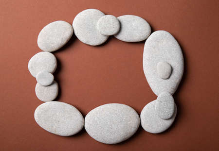 Flat lay view of frame made with flat smooth sea stones on tranquil brown background. Minimalist products background set.の写真素材
