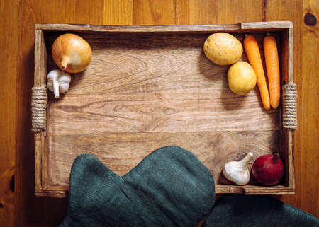 Flat lay view of various root vegetables on wooden tray on kitchen table. Lot of copy space in the center. Carrots, garlic, onion, potatoes.の写真素材