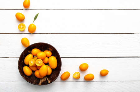 Kumquats or cumquats ( Citrus japonica) inside a coconut bowl and on white wood board background. Citrus food frame border concept with lot of copy space.の写真素材