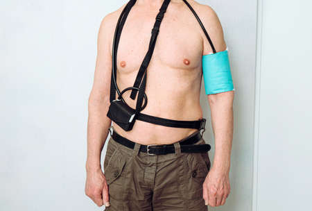 Body of a middle aged man using portable Ambulatory Blood Pressure Monitor (ABPM) for taking...